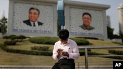 북한 평양의 김일성, 김정일 초상화 앞에서 한 남성이 스마트폰을 사용하고 있다. (자료사진)