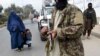 FILE - A burqa-clad woman and a child walk past Taliban fighters along a roadside in Jalalabad, Afghanistan, Dec. 12, 2021.