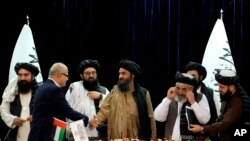 Mullah Abdul Ghani Baradar, Acting Deputy Prime Minister of the Afghan Taliban's caretaker government, center, and the chief financial officer of GAAC Solutions, Razack Aslam Mohammed Abdur Razack, shake hands after signing documents in Kabul, Afghanistan, May 24, 2022.