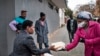 A volunteer for the grassroots charity Hope for Vrededorp reaches out to a woman with a container of home-cooked food, at a daily food distribution in the impoverished district of Vrededorp in Johannesburg, April 28, 2020. 