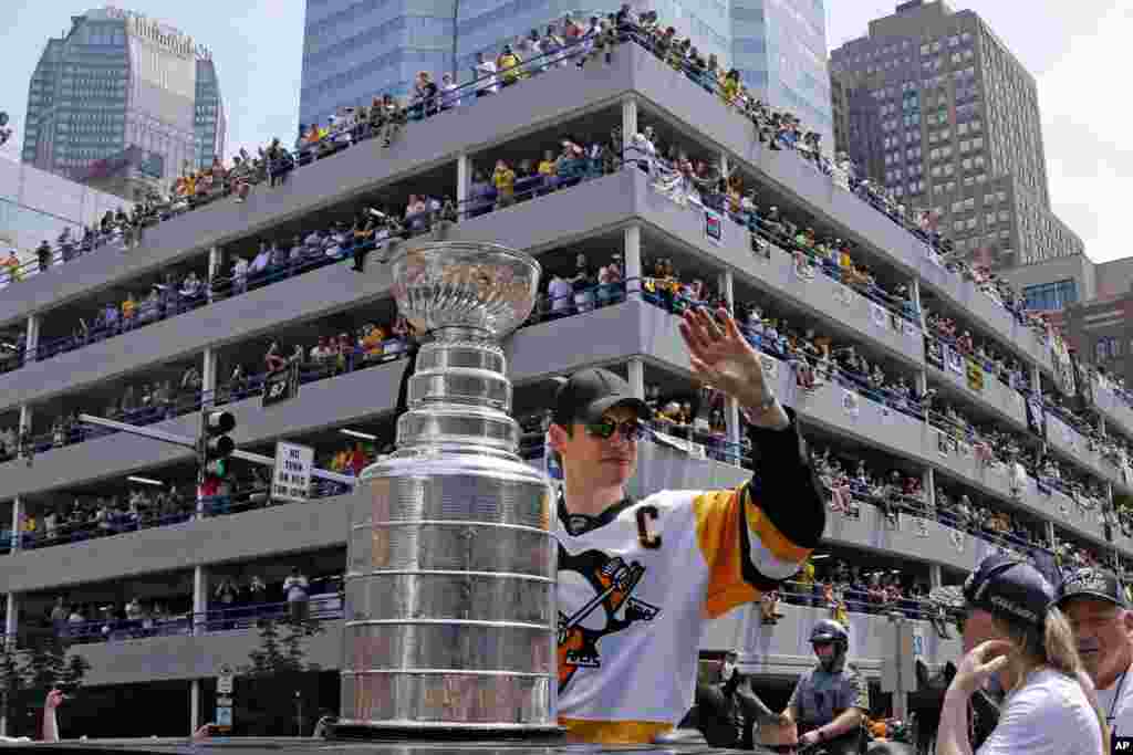 在美国匹茨堡举行的斯坦利杯胜利游行中，匹茨堡企鹅队队员Sidney Crosby 在斯坦利杯（Stanley Cup）旁边挥手致意。（2017年6月14日）