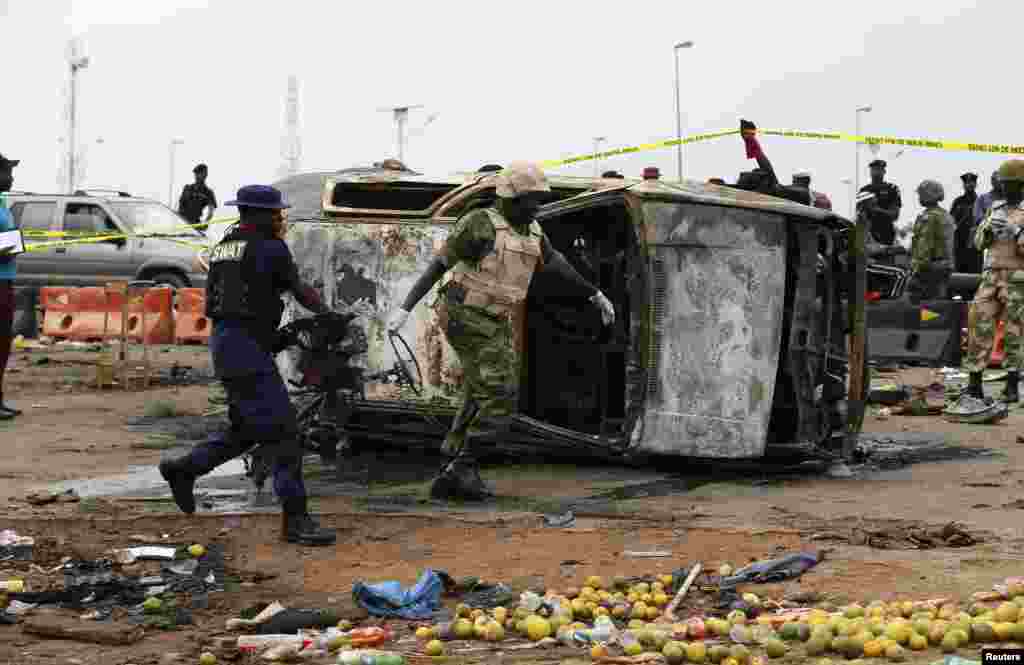 Seorang tentara dan seorang perwira paramiliter membantu memindahkan bagian dari sebuah mobil rusak di lokasi serangan bom mobil di Nyanya, Abuja, Nigeria. &nbsp;