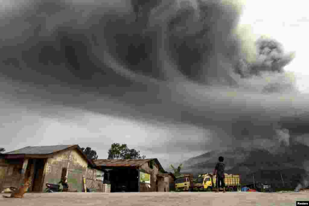 Seorang perempuan memperhatikan Gunung Sinabung memuntahkan abu, terlihat dari desa Sibintun di Karo, Indonesia, 18 November 2013.