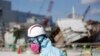 FILE - A Tokyo Electric Power Co. (TEPCO) employee, wearing a protective suit and a mask, walks in front of the No. 1 reactor building at the tsunami-crippled Fukushima Dai-ichi nuclear power plant in Okuma, Fukushima Prefecture, northeastern Japan, Wedne