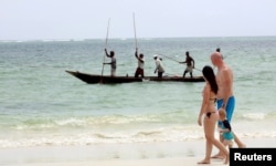 Tourists walk along the beach as fishermen paddle their boat near the shores of the Indian Ocean in Mombasa, Kenya, January 18, 2016.