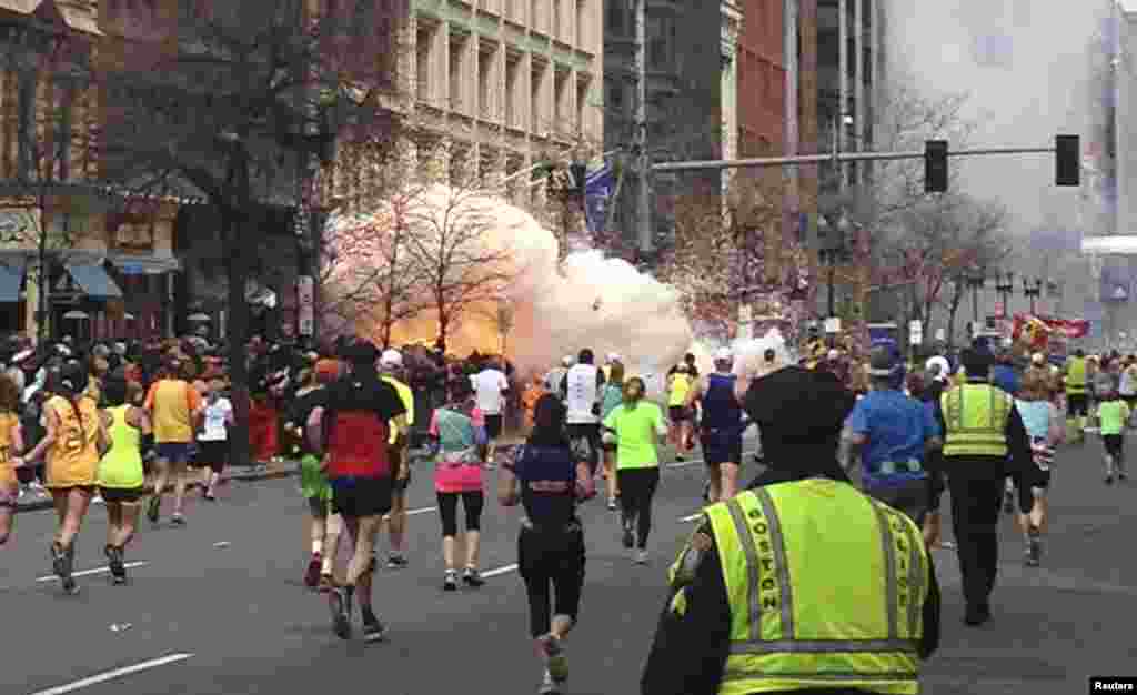 Runners continue to run towards the finish line of the Boston Marathon as an explosion erupts near the finish line of the race, killing 3 people and injuring more than 250, April 15, 2013.