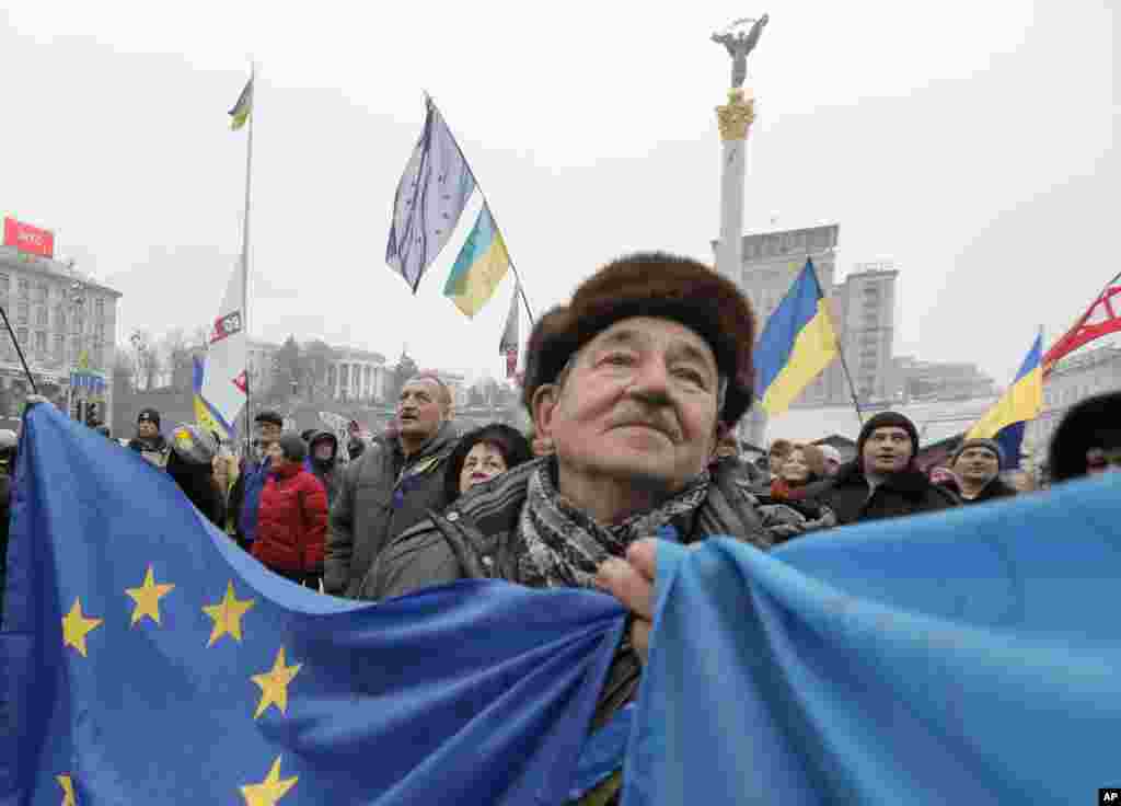 Seorang aktivis Pro - Uni Eropa membentangkan bendera Ukraina dan bendera Uni Eropa melakukan demonstrasi bersama penduduk lainnya di Lapangan Merdeka di Kiev, Ukraina. 